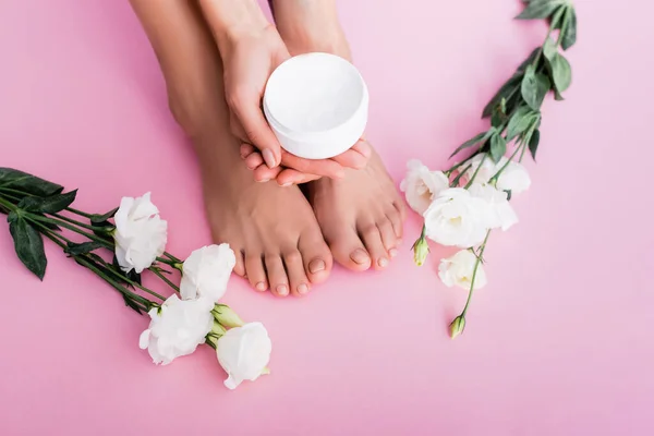 Vue recadrée de la femme tenant crème cosmétique près de fleurs d'eustomie blanches sur fond rose — Photo de stock