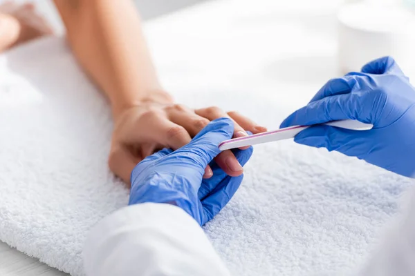 Enfoque selectivo de la lima de uñas en la mano de la manicura haciendo manicura a la mujer, fondo borroso - foto de stock