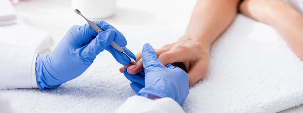 Partial view of manicurist making manicure to client with cuticle pusher, banner — Stock Photo