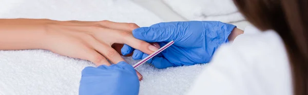 Vista recortada de la manicura usando lima de uñas mientras que hace manicura al cliente, primer plano borroso, bandera - foto de stock