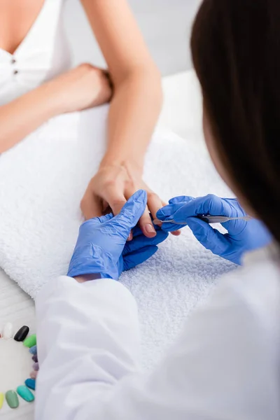 Partial view of manicurist making manicure to client with cuticle pusher, selective focus — Stock Photo