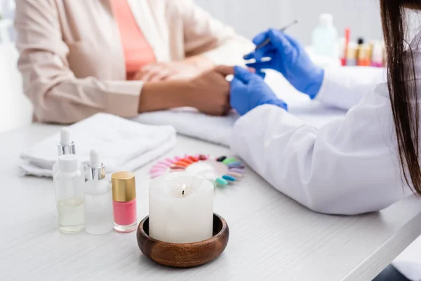 Partial view of manicurist making manicure to woman near candle and manicure supplies on blurred foreground — Stock Photo