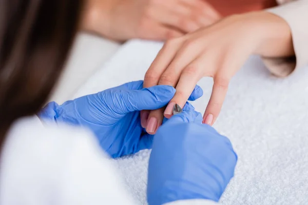 Partial view of manicurist cutting cuticle with nipper while making manicure to woman, blurred foreground — Stock Photo