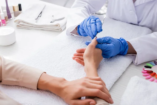 Vista parcial de la manicura en guantes de látex usando empujador de cutícula mientras se hace la manicura al cliente - foto de stock