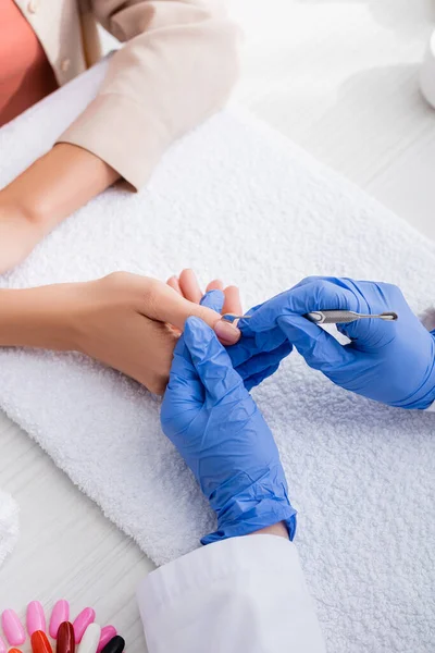 Vista parcial de la manicura hacer manicura al cliente con empujador de cutícula - foto de stock