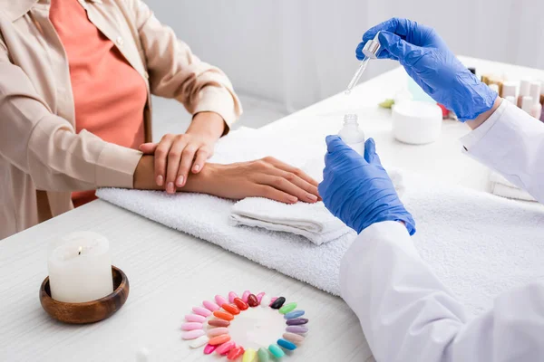 Vista parziale di manicure tenendo cuticola rimozione vicino al cliente e falsi campioni di unghie — Foto stock