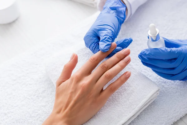 Partial view of manicurist holding cuticle remover while touching finger of client — Stock Photo