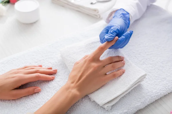 Partial view of manicurist touching finger of woman in nail salon — Stock Photo