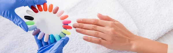 Vista parcial de manicura celebración conjunto de uñas falsas multicolores cerca de la mano del cliente, bandera — Stock Photo