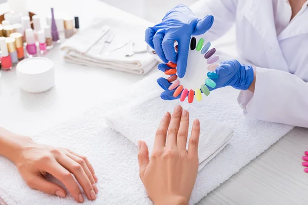 Partial view of manicurist pointing with finger at fake nails palette near client — Stock Photo