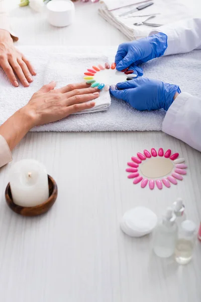 Vista recortada de manicura celebración conjunto de clavos artificiales cerca del cliente y suministros de manicura en primer plano borrosa - foto de stock