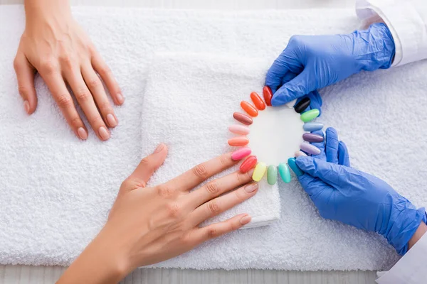 Cropped view of manicurist holding palette of multicolored fake nails near client — Stock Photo