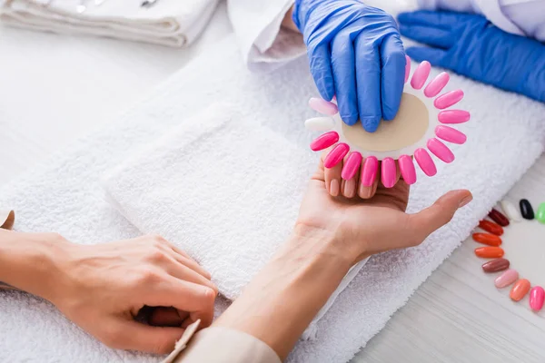 Cropped view of manicurist holding palette of artificial nails near hand of client — Stock Photo