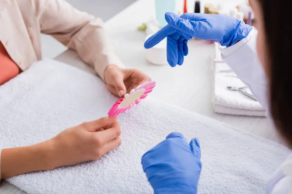 Partial view of manicurist pointing with finger near woman holding palette of fake nails, blurred foreground — Stock Photo