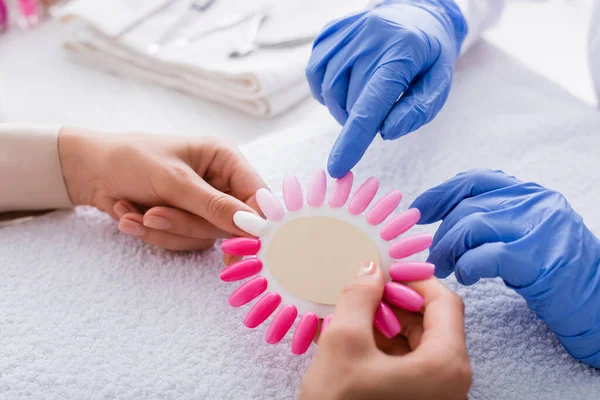 Teilansicht der Maniküre zeigt mit dem Finger auf falsche Nägel Palette in den Händen des Kunden — Stockfoto