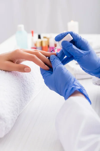Cropped view of manicurist in latex gloves applying nail polish while making manicure to client — Stock Photo