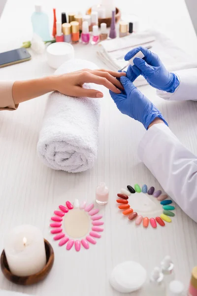 Vista recortada de la manicura aplicando esmalte de uñas mientras se hace la manicura al cliente cerca de uñas falsas y suministros de manicura - foto de stock