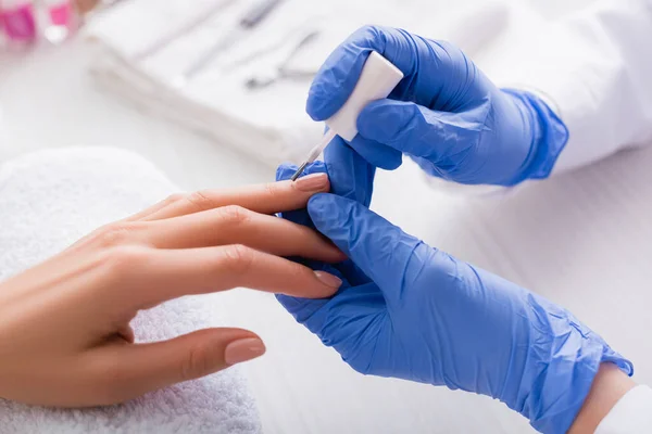 Vista parcial de la manicura en guantes de látex aplicando esmalte en las uñas del cliente - foto de stock