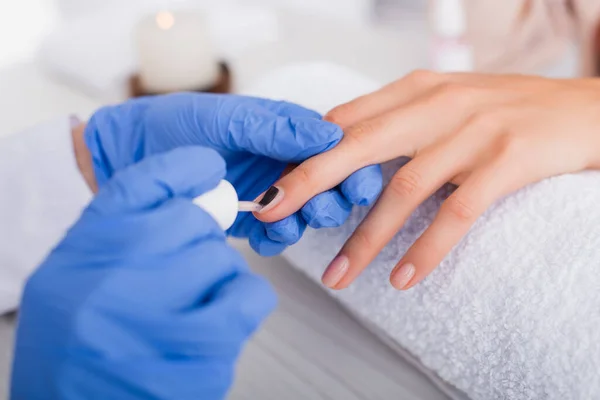 Cropped view of manicurist applying nail varnish on fingernail of client, blurred foreground — Stock Photo