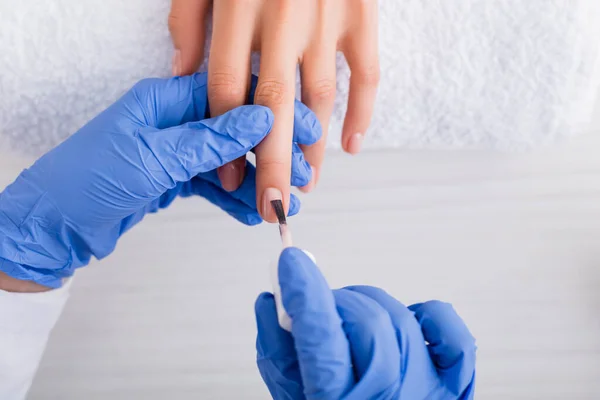 Teilansicht der Maniküre in Latex-Handschuhen, die Nagellack auftragen, während sie Maniküre für den Kunden machen — Stockfoto