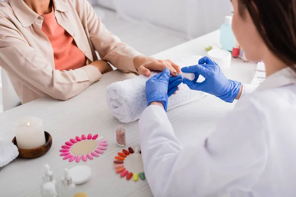 Vista cortada de manicure aplicando esmalte enquanto faz manicure ao cliente perto de vela e unhas artificiais em primeiro plano borrado — Fotografia de Stock