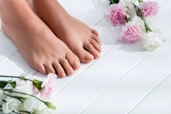 Pés femininos com unhas rosa pastel perto do cravo e flores eustoma na superfície de madeira branca — Fotografia de Stock