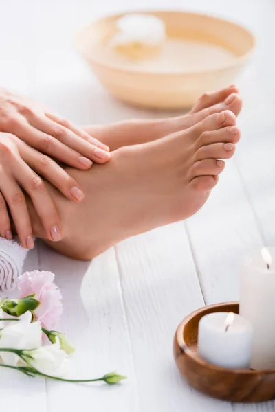 Mani e piedi femminili curati con unghie rosa pastello su una superficie di legno bianca vicino a fiori di eustoma e candele su primo piano sfocate — Foto stock