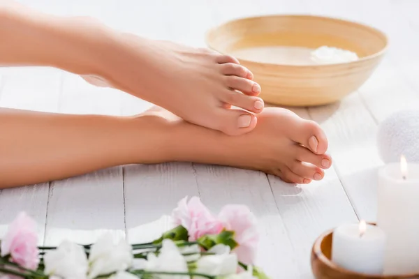 Groomed female feet near bowl on wooden surface near eustoma flowers and candles on blurred foreground — Stock Photo