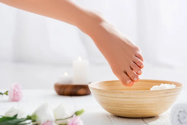 Pied féminin avec ongles rose pastel près du bol et fleurs sur la surface blanche, avant-plan flou — Photo de stock