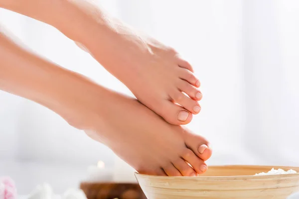 Pés femininos tratados com unhas rosadas brilhantes perto de tigela de madeira no branco — Fotografia de Stock