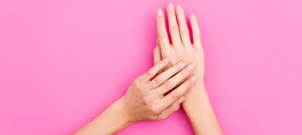 Visão superior de mãos femininas com esmalte de unha pastel em pregos em fundo rosa, bandeira — Fotografia de Stock