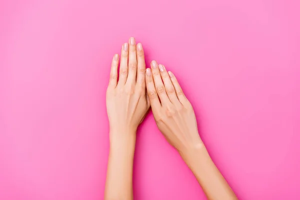 Vista superior de mãos femininas com esmalte pastel em unhas no fundo rosa — Fotografia de Stock