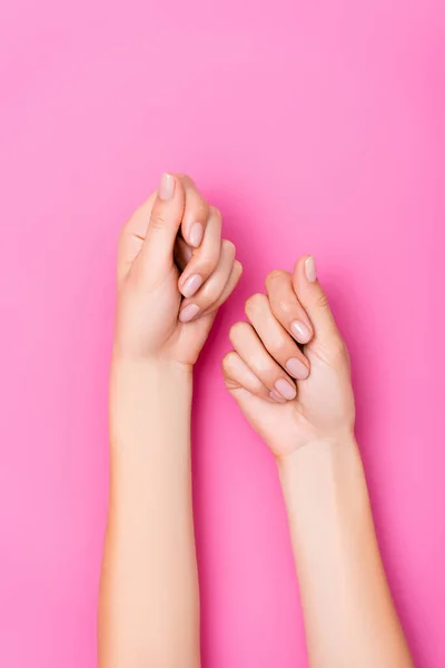 Vue de dessus des mains féminines toilettées avec manucure pastel sur fond rose — Photo de stock