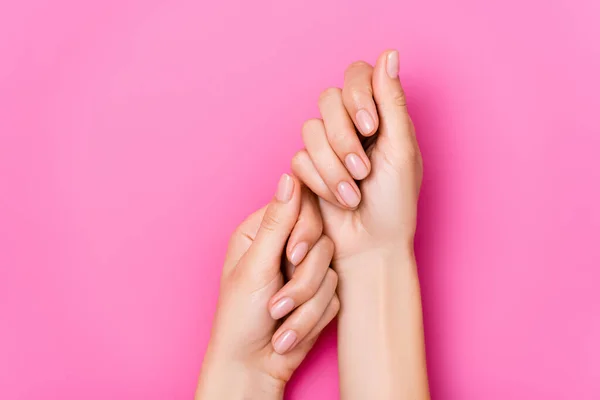 Vista superior de mãos femininas com verniz de unha pastel em unhas no fundo rosa — Fotografia de Stock