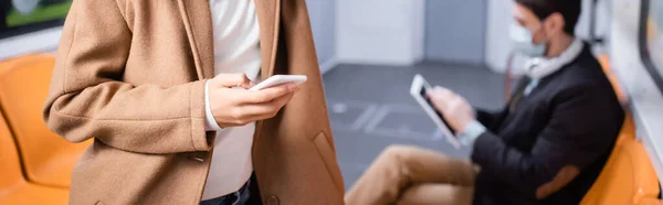 Vista recortada de la joven afroamericana utilizando teléfono inteligente cerca de hombre en el metro sobre fondo borroso, pancarta - foto de stock