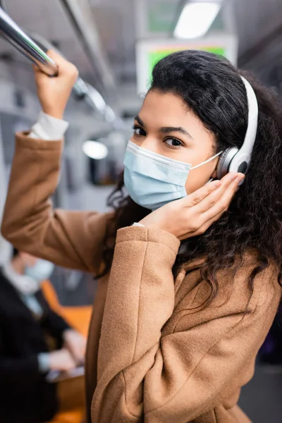 Mujer afroamericana rizada en máscara médica escuchando música en el metro - foto de stock