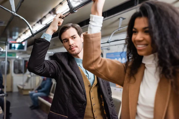 Uomo guardando allegro africano americano donna in metropolitana su sfocato primo piano — Foto stock