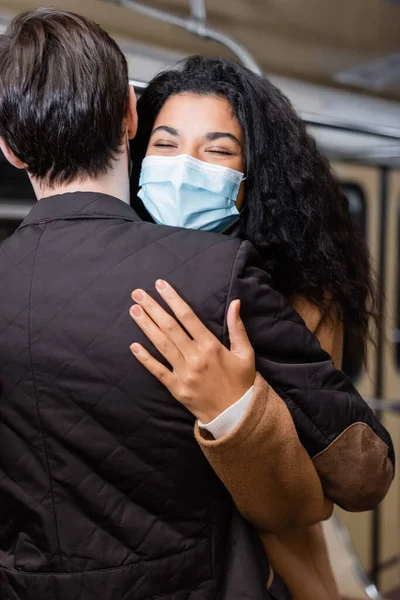 Visão traseira do homem abraçando a namorada afro-americana em máscara médica no metrô — Fotografia de Stock