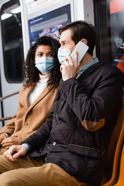 Homme parlant sur smartphone dans le métro près de femme afro-américaine en masque médical — Photo de stock