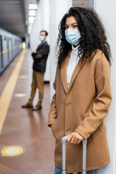 Femme afro-américaine en masque médical debout avec des bagages dans le métro — Photo de stock