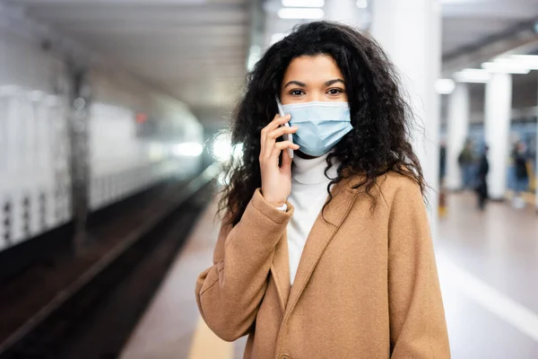 Афроамериканська жінка в медичній масці розмовляє на смартфоні в метро — стокове фото