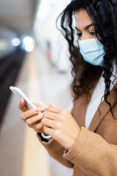 Jeune femme afro-américaine en masque médical en utilisant un smartphone dans le métro — Photo de stock