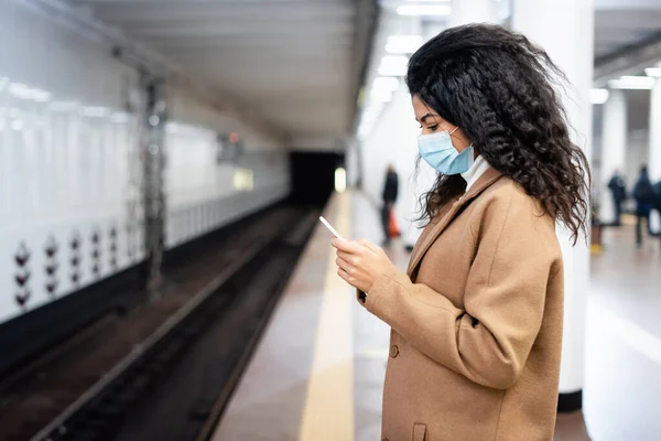 Frisée afro-américaine en masque médical en utilisant un téléphone portable dans le métro — Photo de stock