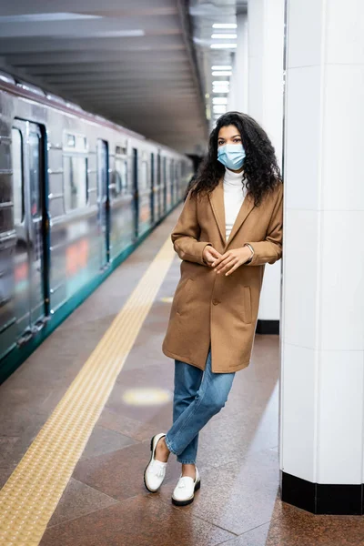 Full length of curly african american woman in medical mask standing in subway — Stock Photo