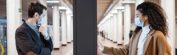 Jeune femme afro-américaine et l'homme dans des masques médicaux près du stand d'information dans le métro, bannière — Photo de stock