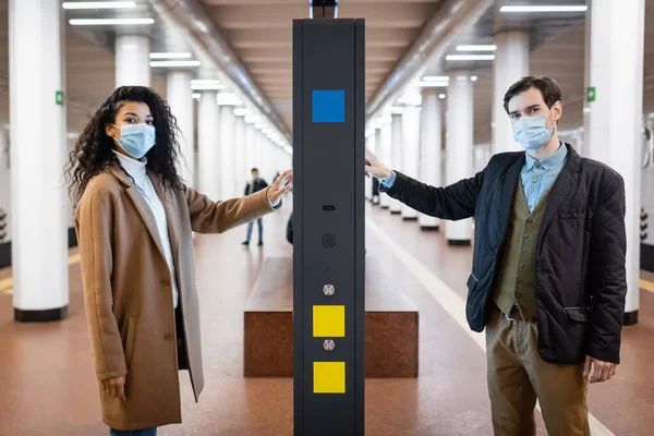 Femme afro-américaine bouclée et l'homme dans des masques médicaux près stand d'information dans le métro — Photo de stock