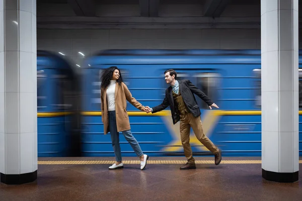 Flou de mouvement du couple interactionnel tenant la main tout en marchant près du wagon dans le métro — Photo de stock