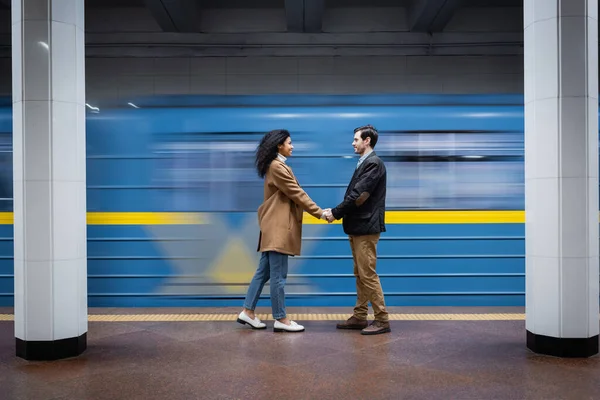 Longue exposition du couple interactionnel tenant la main tout en se tenant près du wagon dans le métro — Photo de stock