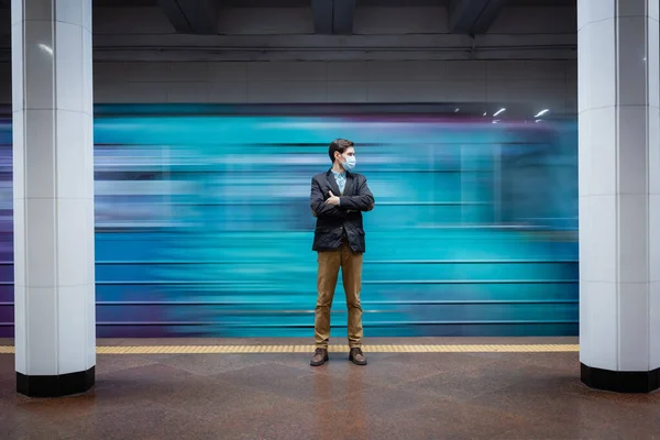 Motion blur of man in medical mask standing with crossed arms near passing wagon in subway — Stock Photo