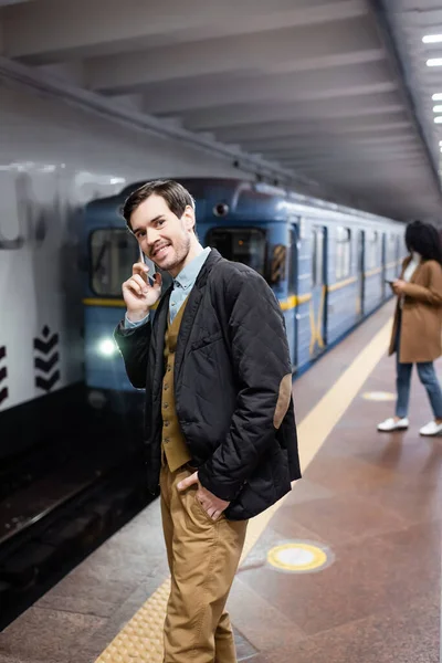 Homem feliz falando no smartphone perto de mulher americana africana e vagão de metro no fundo borrado — Fotografia de Stock